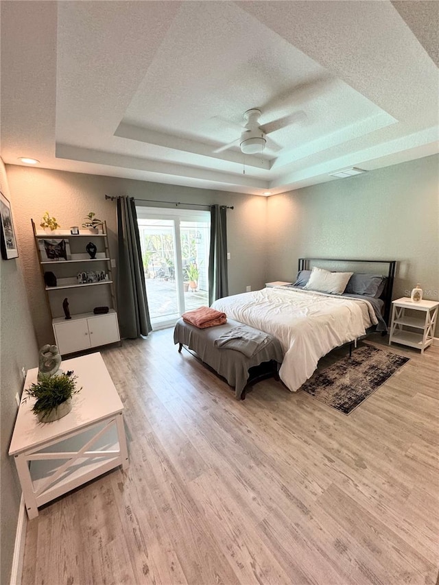 bedroom featuring access to outside, a tray ceiling, a textured ceiling, wood finished floors, and a textured wall