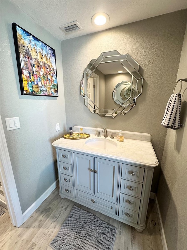 bathroom featuring vanity, wood finished floors, visible vents, baseboards, and a textured wall