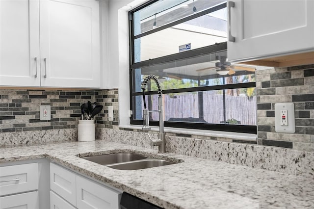 kitchen featuring light stone countertops, a sink, ceiling fan, white cabinetry, and tasteful backsplash