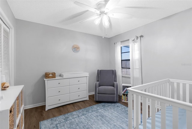 bedroom with a ceiling fan, wood finished floors, a closet, a nursery area, and baseboards