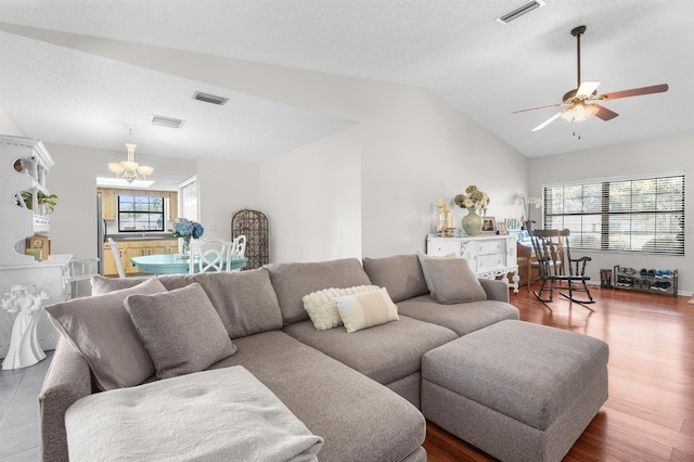 living area featuring vaulted ceiling, visible vents, ceiling fan with notable chandelier, and wood finished floors