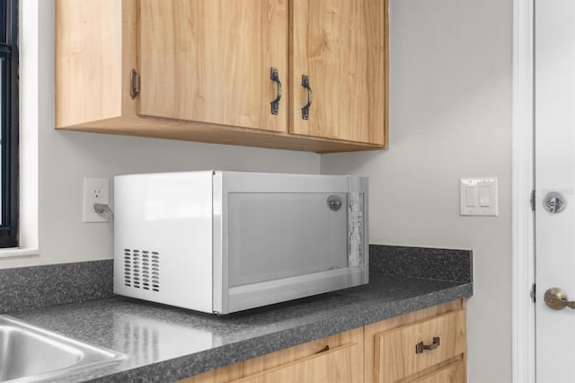 details featuring white microwave, dark countertops, and light brown cabinetry