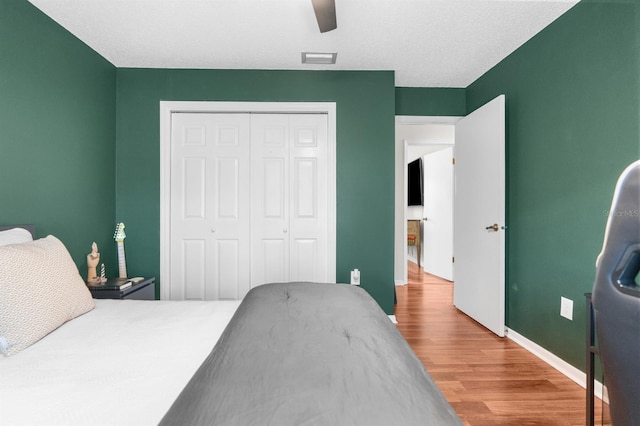 bedroom with visible vents, a ceiling fan, wood finished floors, a closet, and baseboards