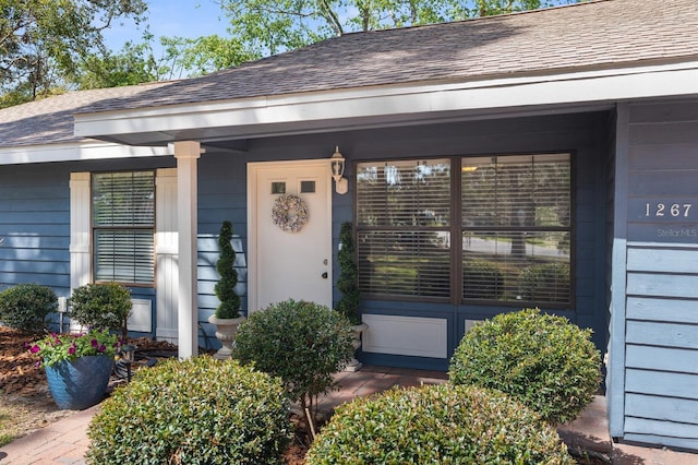 view of exterior entry featuring roof with shingles