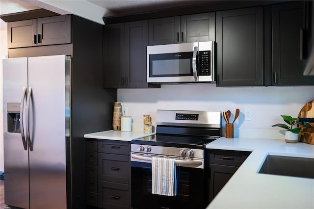 kitchen featuring a sink, stainless steel appliances, light countertops, and dark cabinets