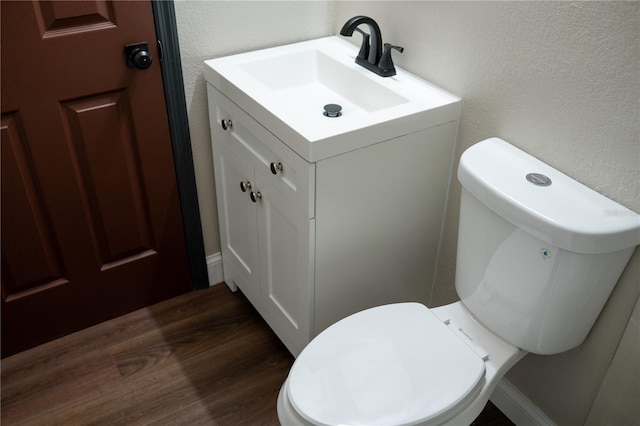 half bath with wood finished floors, toilet, vanity, and a textured wall