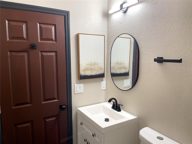 bathroom featuring vanity, toilet, and a textured wall