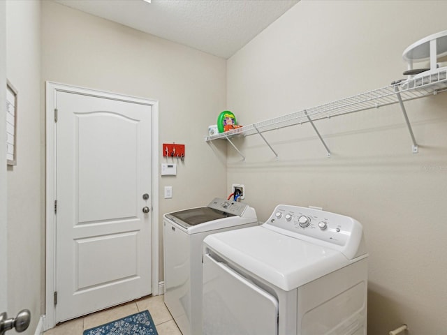 clothes washing area featuring light tile patterned floors, a textured ceiling, laundry area, and washer and clothes dryer