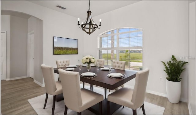 dining area with light wood-type flooring, visible vents, arched walkways, and baseboards