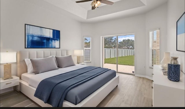 bedroom with access to exterior, baseboards, wood finished floors, a raised ceiling, and a ceiling fan