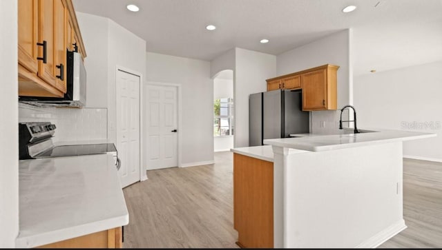 kitchen featuring a peninsula, arched walkways, a sink, light wood-style floors, and appliances with stainless steel finishes