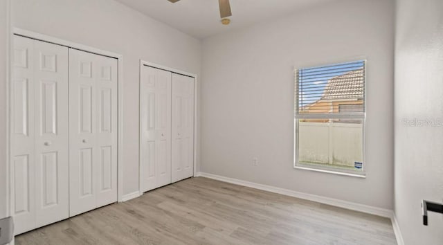 unfurnished bedroom with baseboards, two closets, wood finished floors, and a ceiling fan