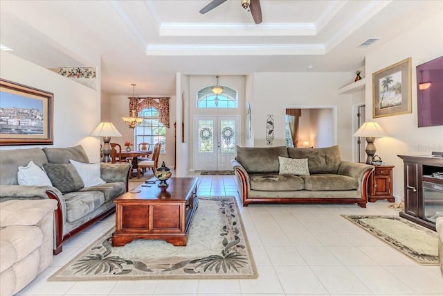 living area with a raised ceiling, ceiling fan with notable chandelier, visible vents, and ornamental molding