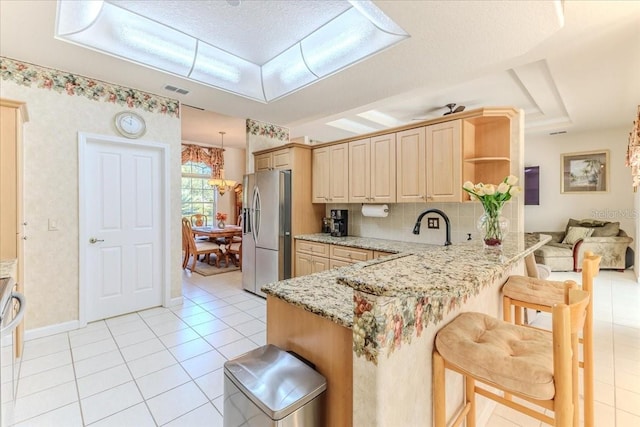 kitchen with a kitchen bar, stainless steel fridge, a peninsula, light tile patterned flooring, and light stone countertops