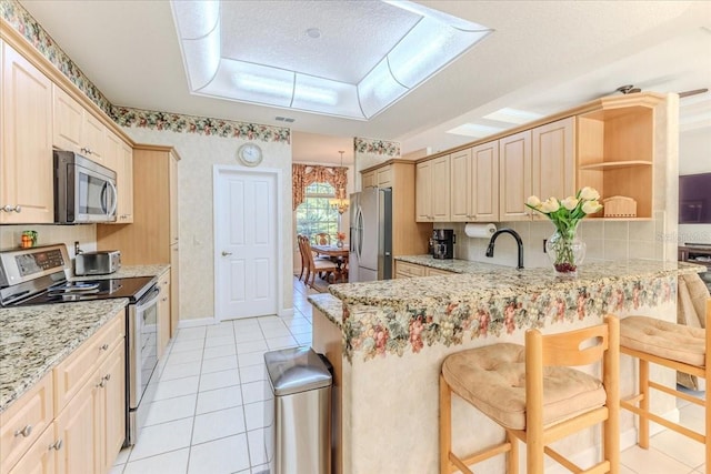 kitchen with a peninsula, light tile patterned floors, light stone countertops, and stainless steel appliances