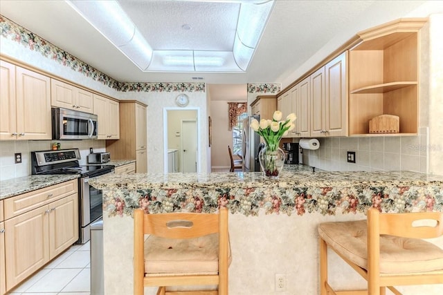 kitchen with a kitchen bar, a peninsula, light tile patterned flooring, and appliances with stainless steel finishes