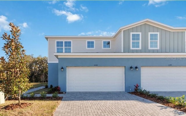 view of property featuring board and batten siding, decorative driveway, a garage, and stucco siding