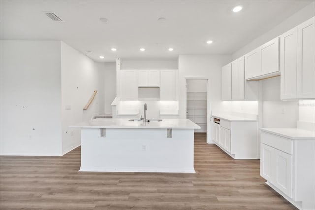 kitchen featuring visible vents, a sink, light wood-style flooring, white cabinets, and a kitchen island with sink