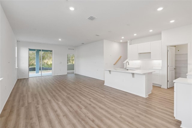 kitchen featuring visible vents, open floor plan, recessed lighting, white cabinets, and a sink