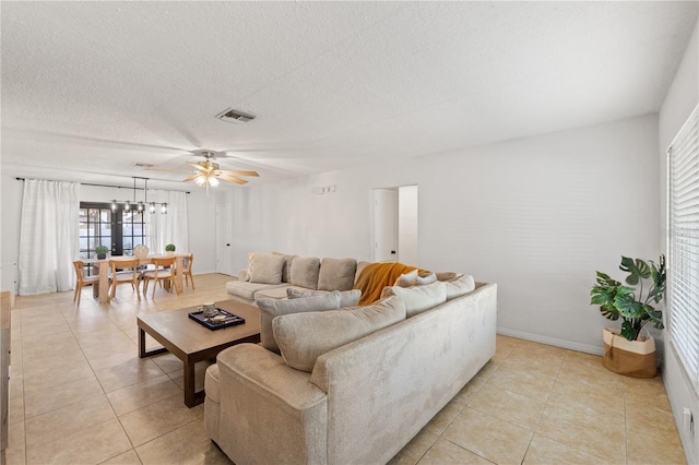 living area featuring light tile patterned floors, visible vents, ceiling fan with notable chandelier, and a textured ceiling