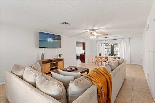 living area featuring light tile patterned flooring, ceiling fan with notable chandelier, visible vents, and a textured ceiling