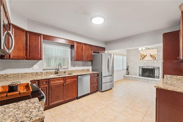 kitchen with light stone countertops, a sink, appliances with stainless steel finishes, a brick fireplace, and backsplash