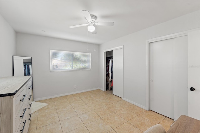 bedroom featuring light tile patterned floors, two closets, baseboards, and a ceiling fan