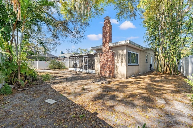 rear view of property featuring a chimney, concrete block siding, a fenced backyard, and a sunroom