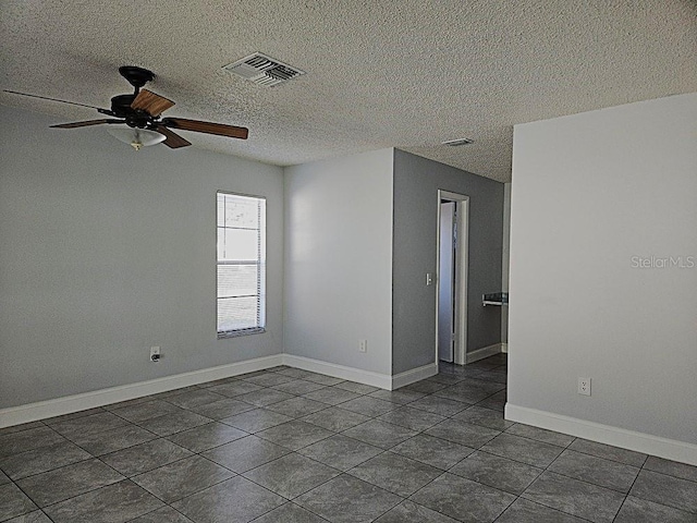 empty room featuring a ceiling fan, visible vents, baseboards, dark tile patterned flooring, and a textured ceiling