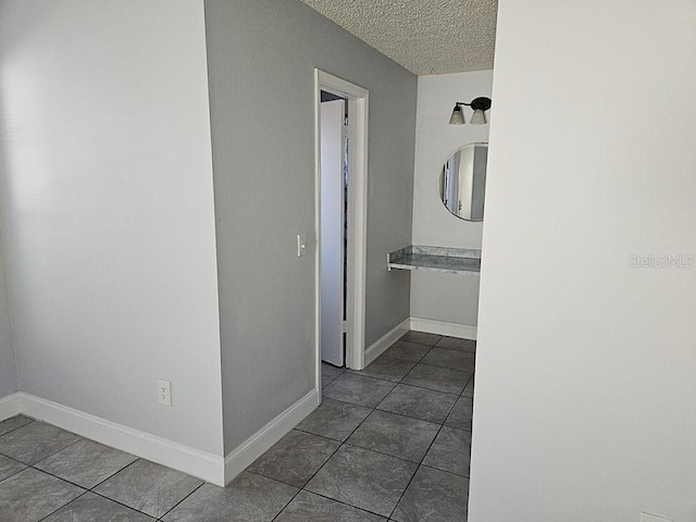 hall featuring tile patterned flooring, a textured ceiling, and baseboards