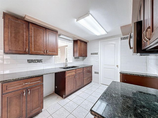 kitchen featuring light tile patterned flooring, backsplash, dark stone counters, and a sink