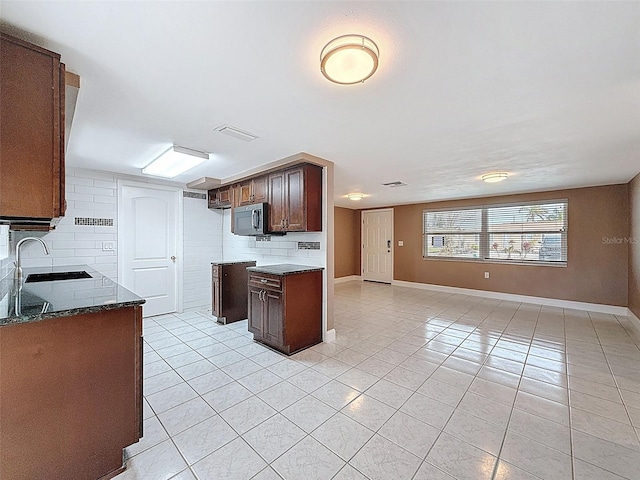 kitchen featuring decorative backsplash, stainless steel microwave, light tile patterned flooring, and a sink