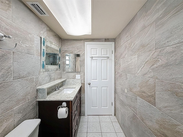 bathroom featuring vanity, visible vents, tile patterned flooring, tile walls, and toilet