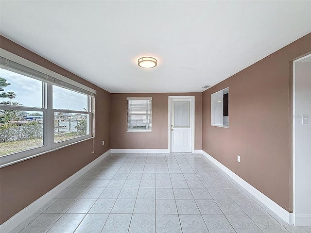 empty room featuring light tile patterned flooring, visible vents, and baseboards