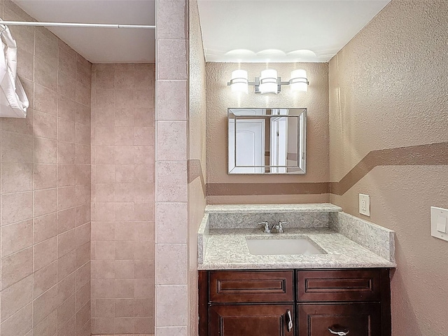 full bathroom with vanity, a textured wall, and a tile shower