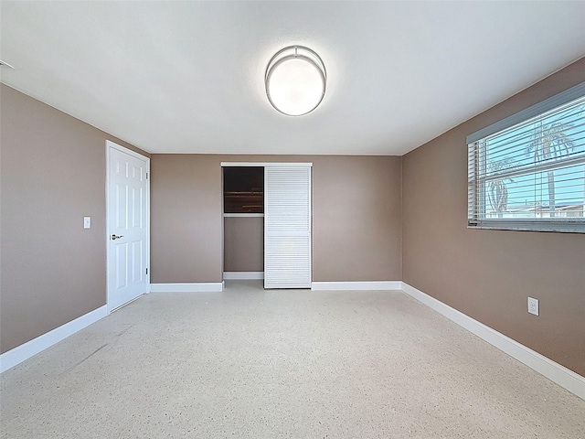 unfurnished bedroom with speckled floor, baseboards, and a closet