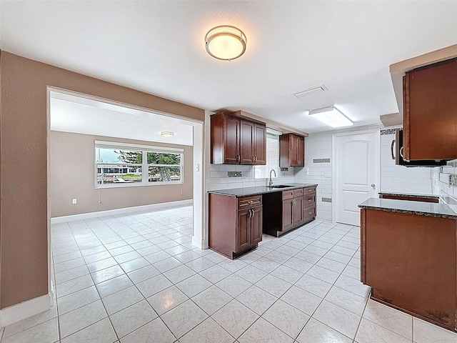 kitchen with a sink, backsplash, light tile patterned flooring, and black dishwasher