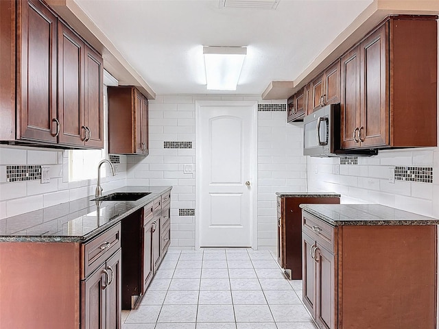 kitchen with a sink, stainless steel microwave, tasteful backsplash, dark stone counters, and light tile patterned flooring