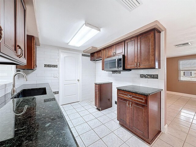 kitchen with a sink, stainless steel microwave, visible vents, and dark stone counters