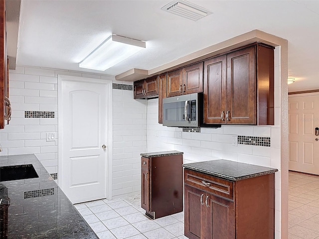 kitchen with stainless steel microwave, visible vents, dark brown cabinetry, dark stone counters, and light tile patterned floors