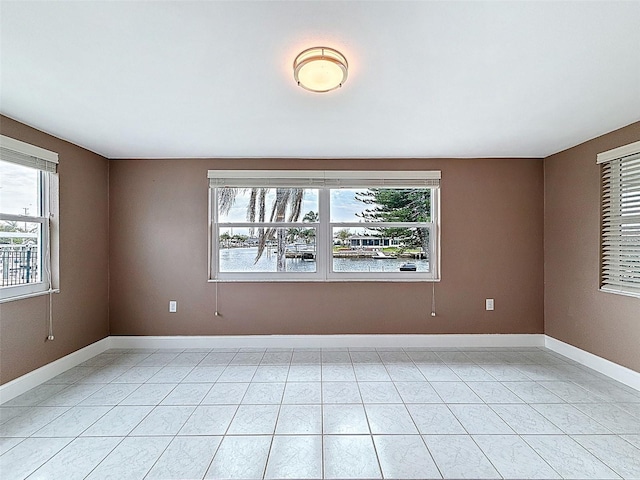 empty room featuring light tile patterned floors, a healthy amount of sunlight, and baseboards