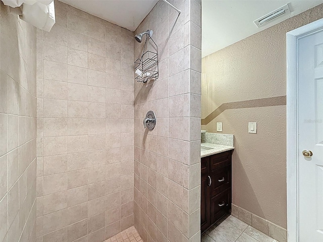 full bath with vanity, a textured wall, visible vents, and a tile shower