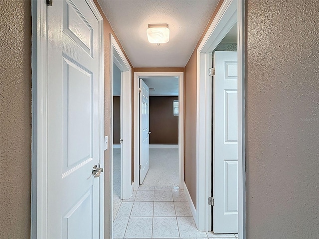 corridor with light tile patterned flooring, a textured wall, baseboards, and a textured ceiling