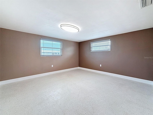 unfurnished room featuring speckled floor, visible vents, and baseboards