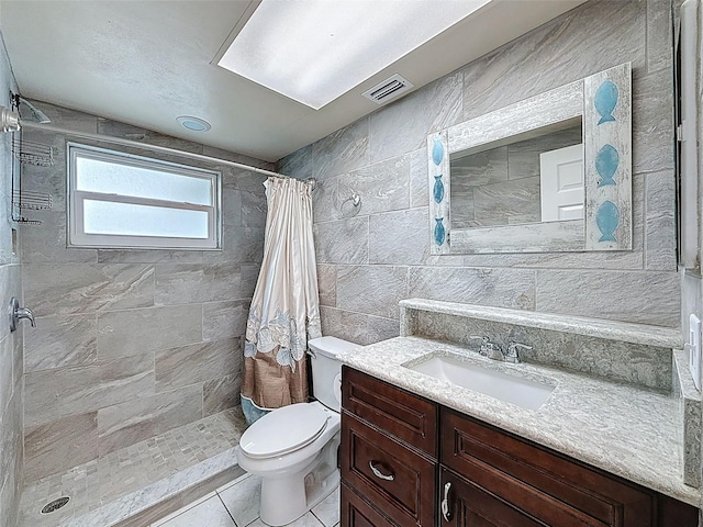 bathroom featuring vanity, visible vents, a tile shower, tile walls, and toilet