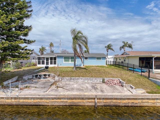 rear view of house featuring a yard, fence, a water view, and a sunroom