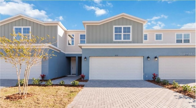 multi unit property featuring stucco siding, an attached garage, decorative driveway, and board and batten siding