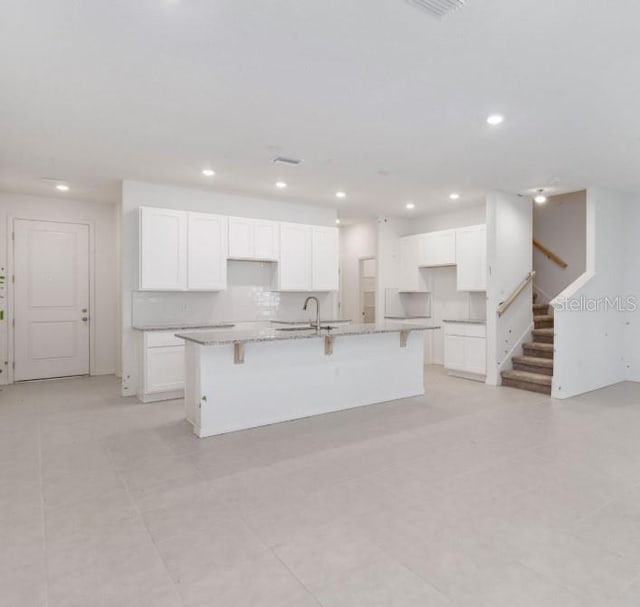 kitchen with a large island, recessed lighting, white cabinetry, and a sink