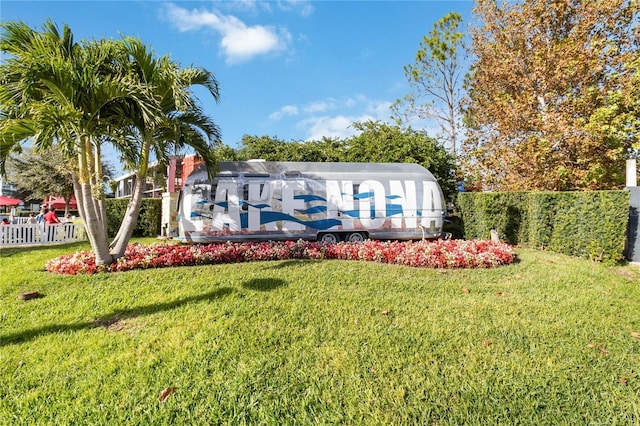 community / neighborhood sign featuring a yard and fence