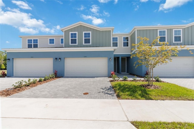 view of front of home featuring an attached garage, decorative driveway, board and batten siding, and stucco siding